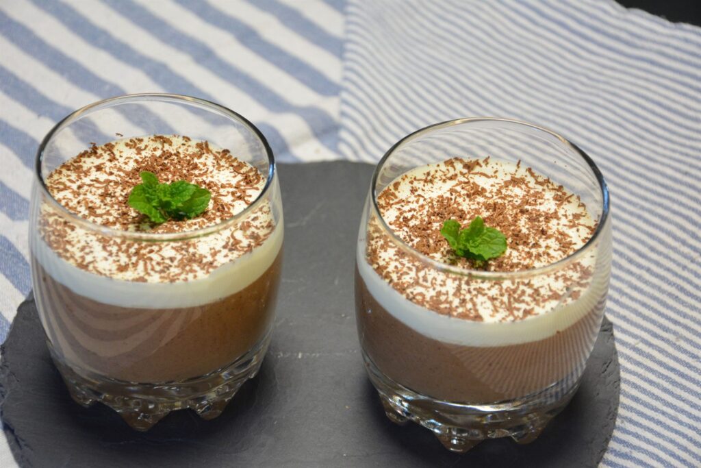 To glas hjemmelavet chokolademousse toppet med flødeskum, revet chokolade og friske mynteblade