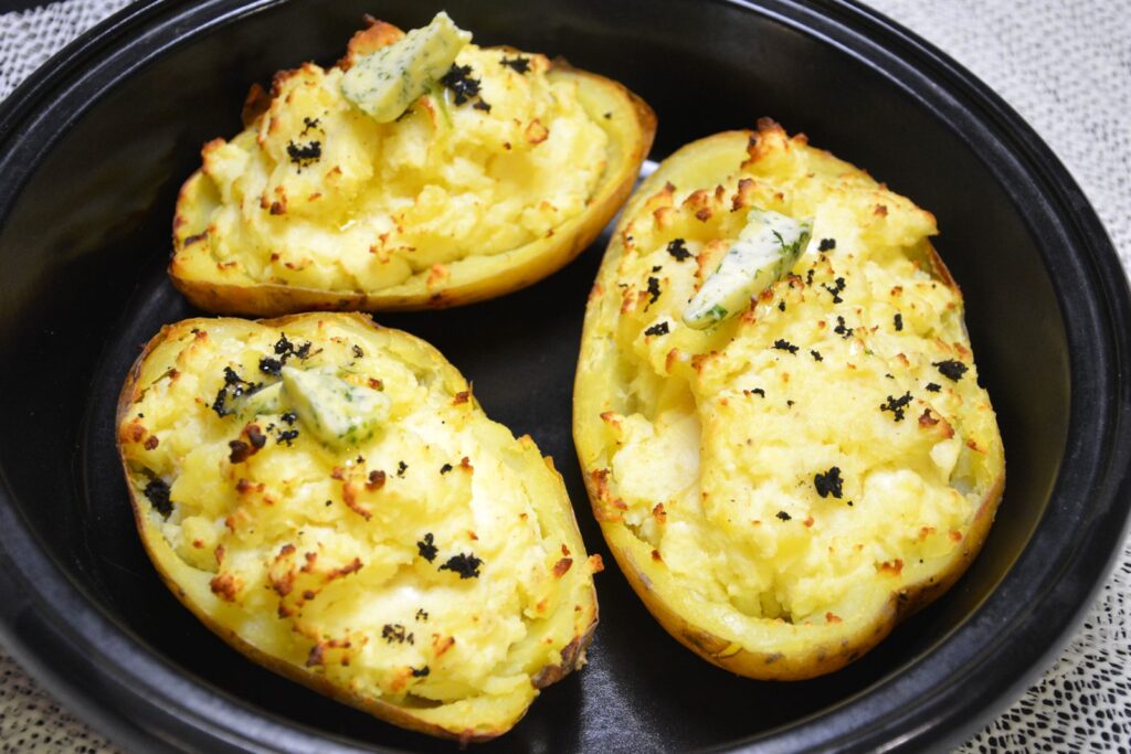 Dobbeltbagte bagekartofler med feta, revet trøffel og krydderurtesmør i et sort fad