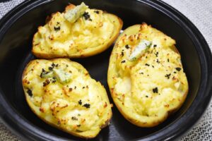 Dobbeltbagte bagekartofler med feta, revet trøffel og krydderurtesmør i et sort fad