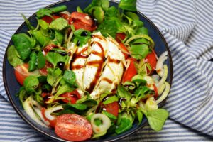 Burrata-salat med halve cherrytomater i flere farver, babyspinat, rødløg og balsamicoglaze på et fad