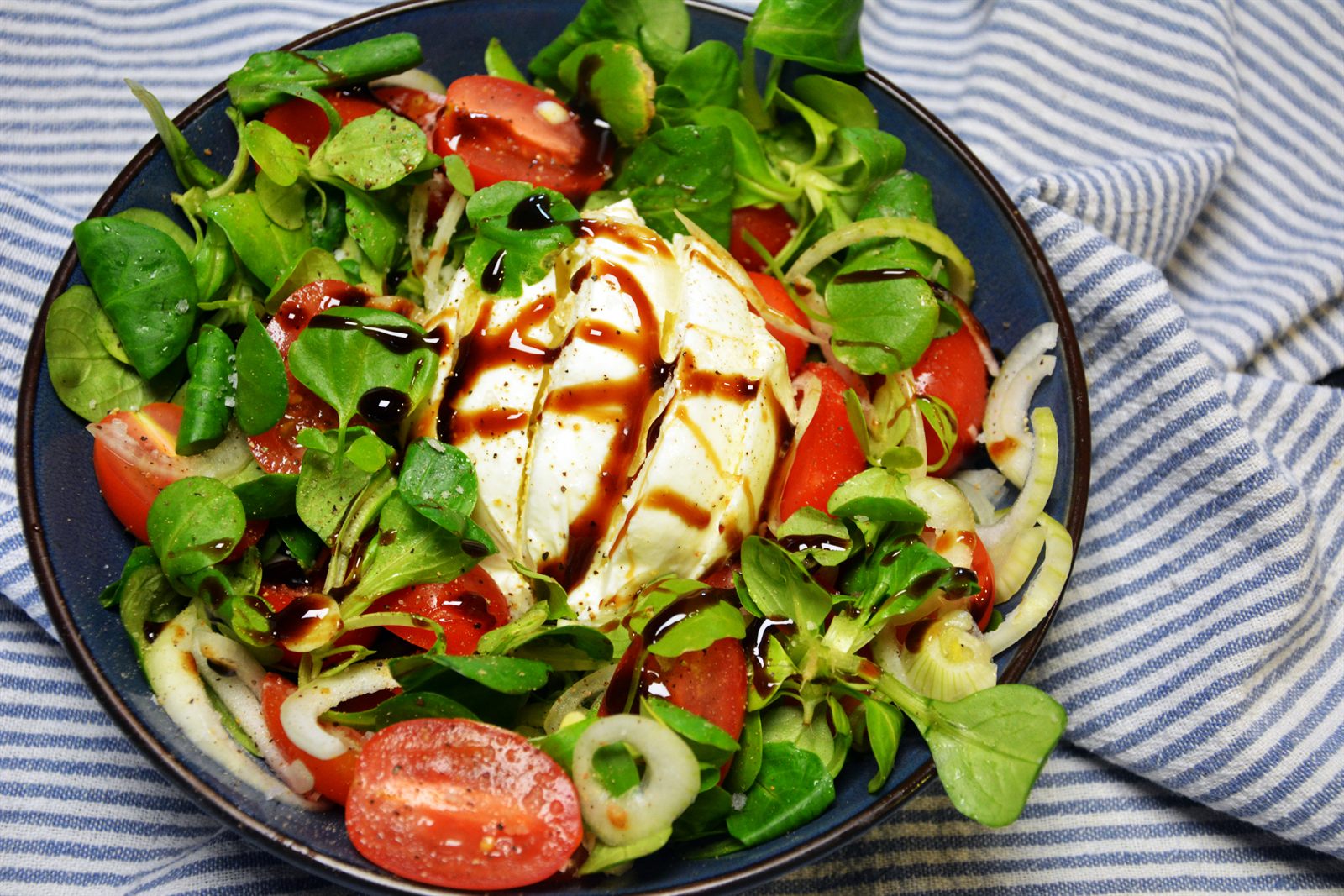 Burrata-salat med halve cherrytomater i flere farver, babyspinat, rødløg og balsamicoglaze på et fad