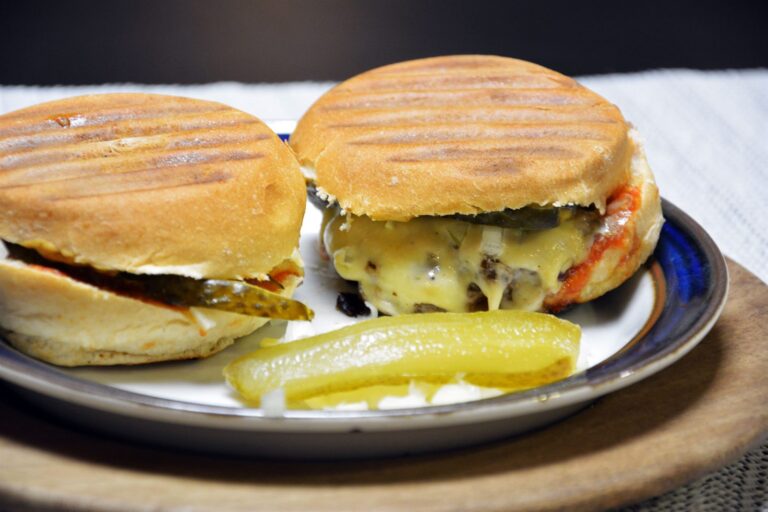 To hjemmelavede cheeseburgere med grillstriber på bollen, smeltet ost og syltet drueagurk på en tallerken