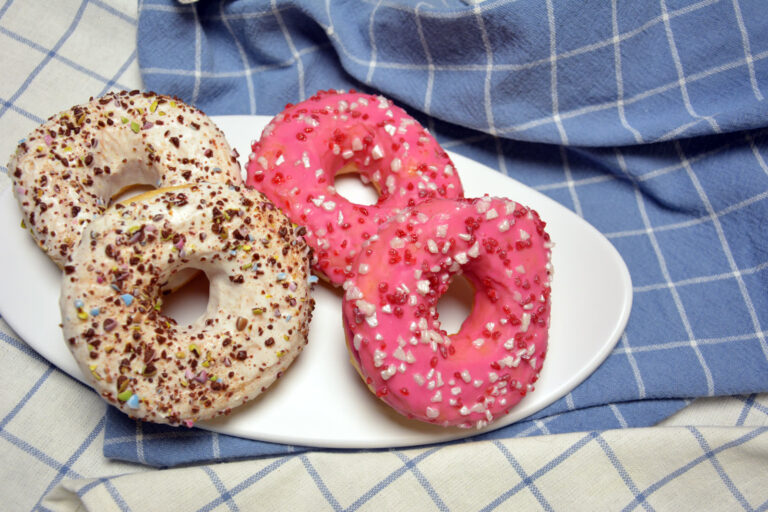 Hjemmelavede donuts med lyserød og hvid glasur og farvet krymmel på et fad