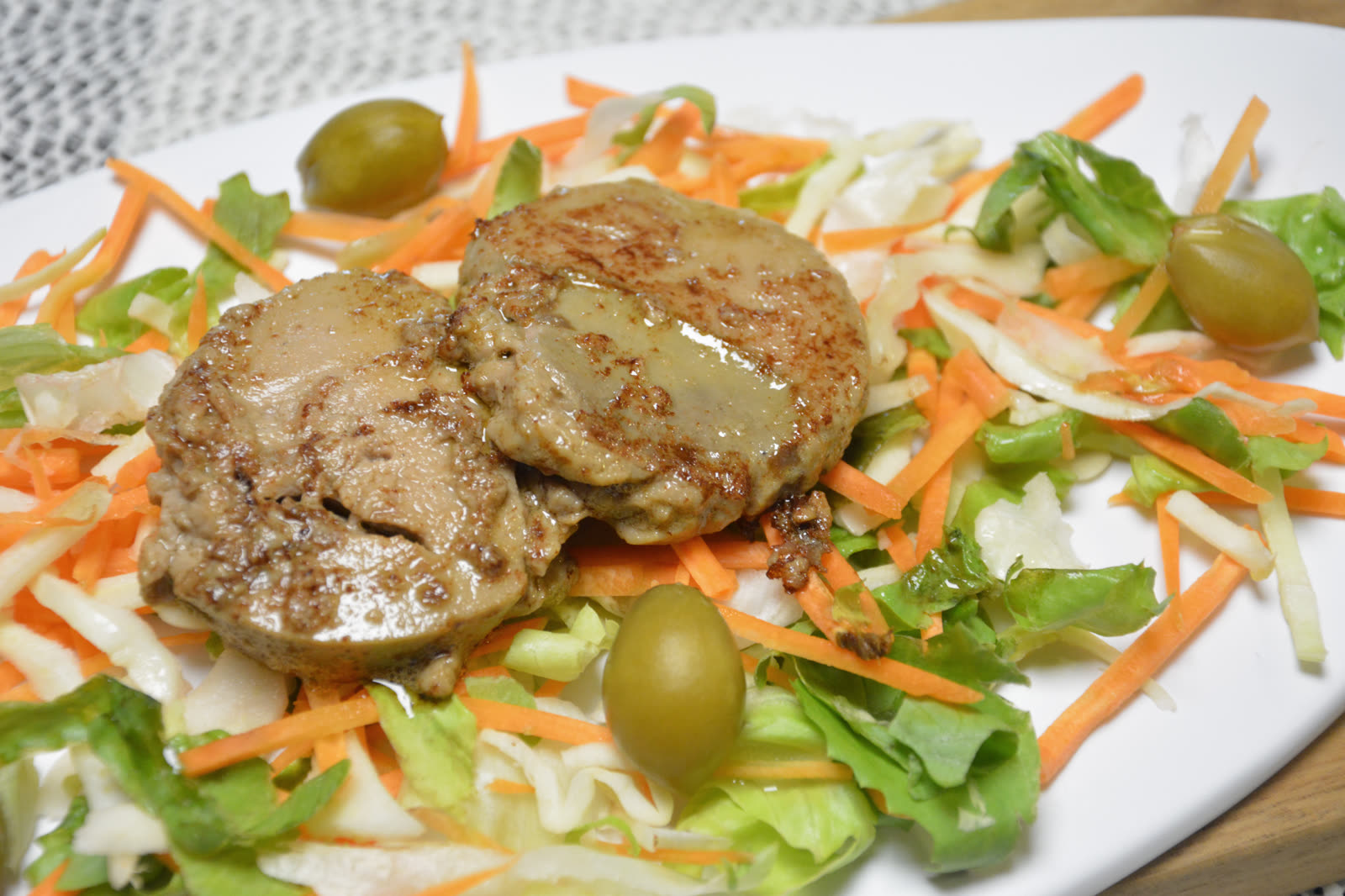 Stegt foie gras i to runde skiver lagt på en bund af blandet salat med gulerod, hvidkål og grønne babyferskner