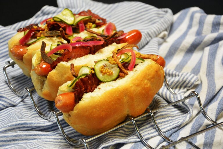 Gourmet hotdog i flækket pølsebrød med bacon, syltede rødløg, ristede løg, agurkesalat og syltede sennepsfrø