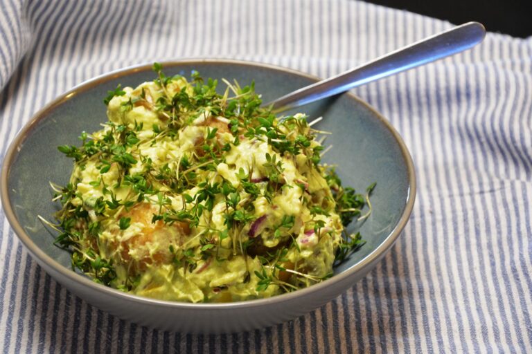 Grøn kartoffelsalat med avocado, rygeost og rødløg i en blå skål, dækket af friskklippet karse