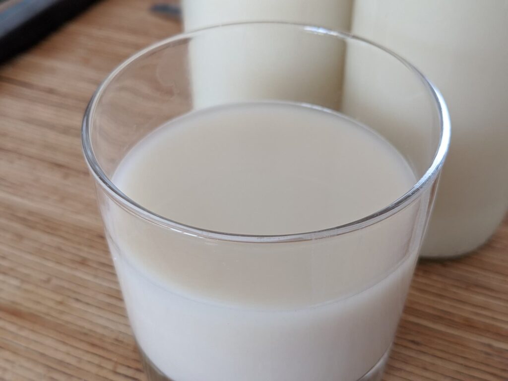 Glas hjemmelavet havremælk med flaske havremælk i baggrunden på et træbord