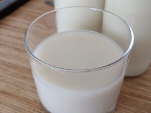 Glas hjemmelavet havremælk med flaske havremælk i baggrunden på et træbord