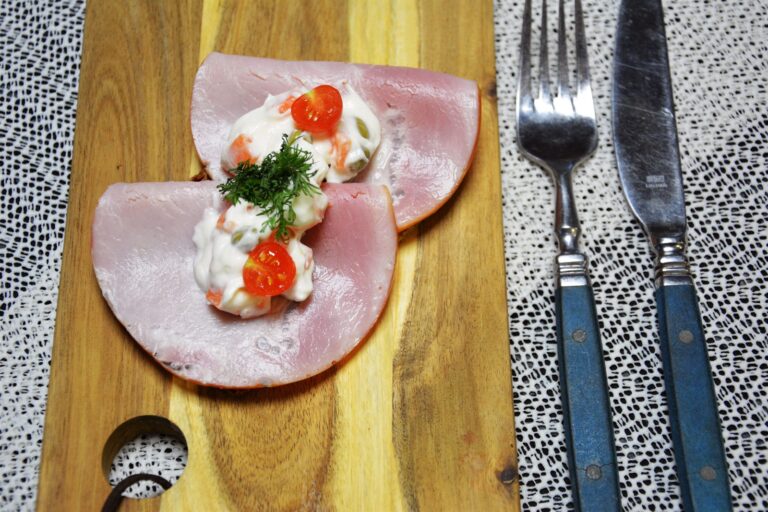 Italiensk salat med gulerodstern og ærter lagt oven på to foldede skiver kogt skinke på rugbrød, pyntet med en halv cherrytomat og dild, på et træskærebræt