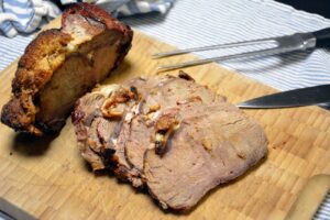 Grillet kalvefilet med sprødt, ruderidset fedtlag på et lyst skærebræt, delvis skåret i skiver med lys, let rosa midte, forskærerkniv og gaffel ved siden af