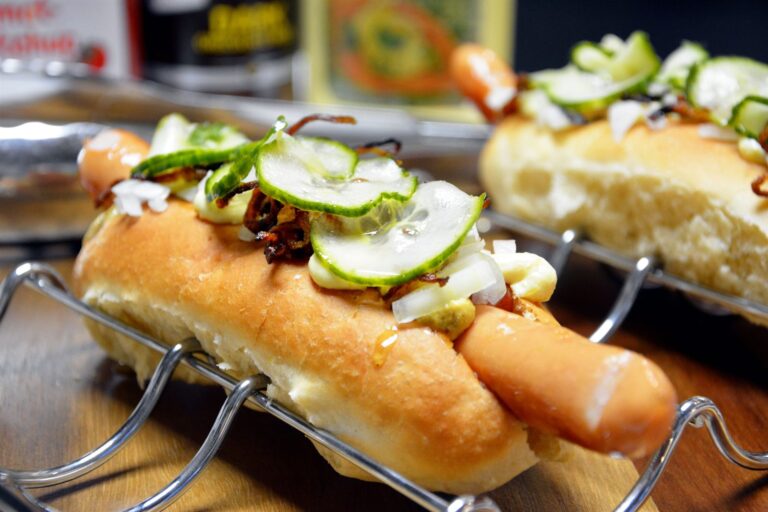 Ristet hotdog i hjemmebagt pølsebrød flækket ovenfra, med sennep, remoulade, rå løg, ristede løg og skiver af agurkesalat
